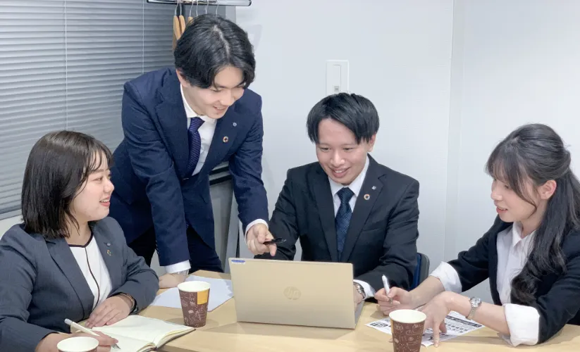 4人の男女がパソコンを囲んで会議している写真